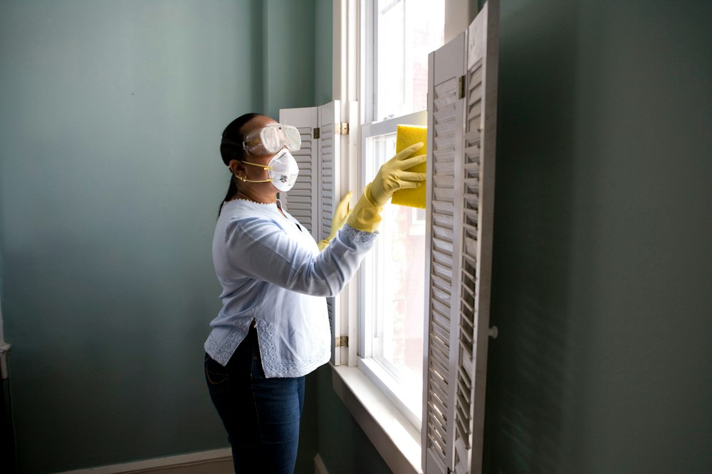 A person in a mask and gloves cleaning a window